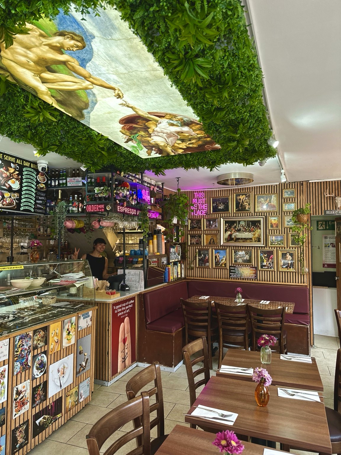 Interno di Artist Cafe London con pareti decorate con opere d’arte, piante e tavoli in legno